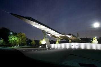 A retired A-12 Oxcart mounted on the ground, lit from beneath at night.